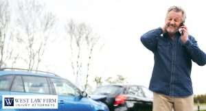 Man holding his neck while calling after a car accident, with damaged vehicles behind him for a personal injury attorney claim